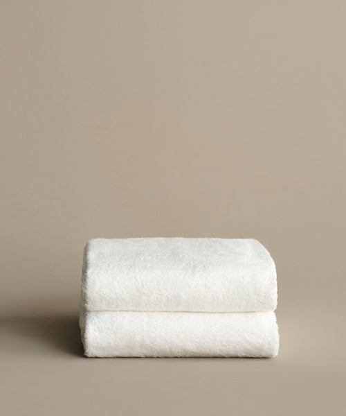 A single Loom Bath Towel, super-soft and white, is folded and placed against a simple light beige background.