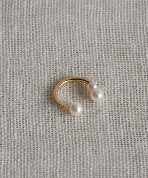 The Loren Pearl Ear Cuff, featuring two freshwater pearls on each end of a gold open design, is styled against a textured off-white fabric background.
