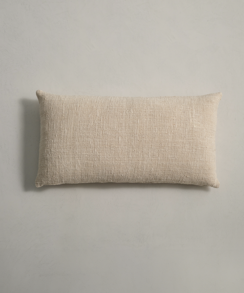 The Luna Lumbar Pillow, featuring a handwoven design and feather down insert, rests elegantly on a white surface.