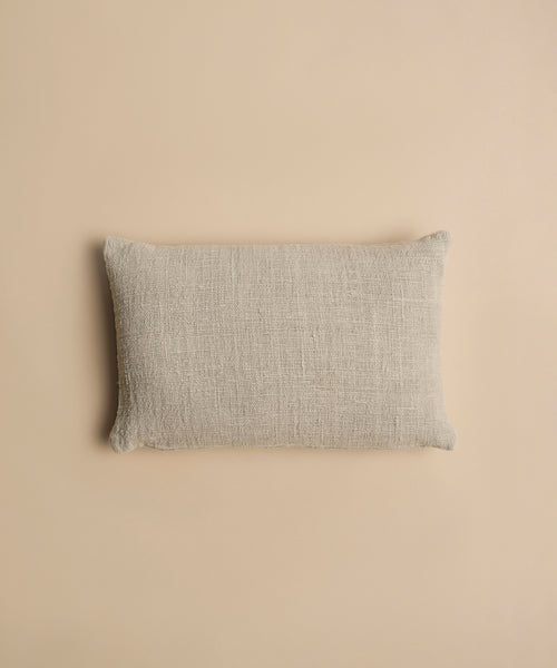 The Luna Lumbar Pillow, featuring a rectangular shape and textured beige fabric, lies flat on a matching beige surface in a top-down view.