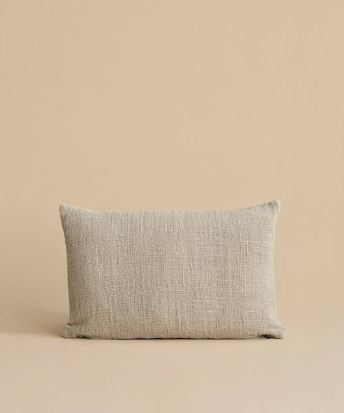 The Luna Lumbar Pillow, featuring a textured beige fabric cover and feather down insert, is placed against a matching beige background.