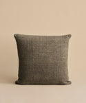 The Luna Pillow, a square dark gray handwoven cushion with a feather down insert, is placed against a simple light beige background.