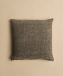 The Luna Pillow is a square, textured dark gray cotton pillow with a visible fabric weave and feather down insert, shown on a plain beige background.