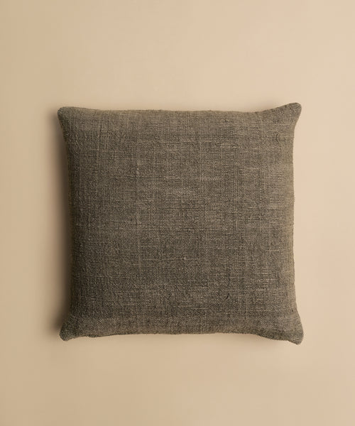 The Luna Pillow is a square, textured dark gray cotton pillow with a visible fabric weave and feather down insert, shown on a plain beige background.