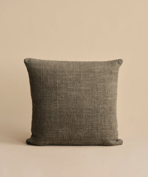 The Luna Pillow, a square dark gray handwoven cushion with a feather down insert, is placed against a simple light beige background.