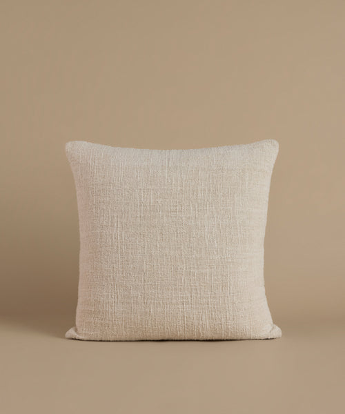A textured cream color pillow against a beige background.