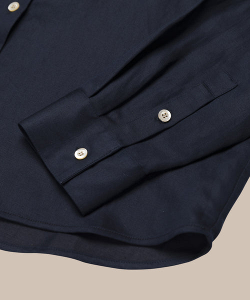 A close-up of the Madeline Shirt highlights its navy linen texture and white buttons, set against a neutral beige background.