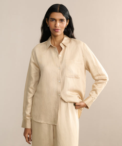A person with long black hair, wearing the spring-ready Madeline Shirt in a subtle linen texture, stands against a neutral background with one hand in their pocket.