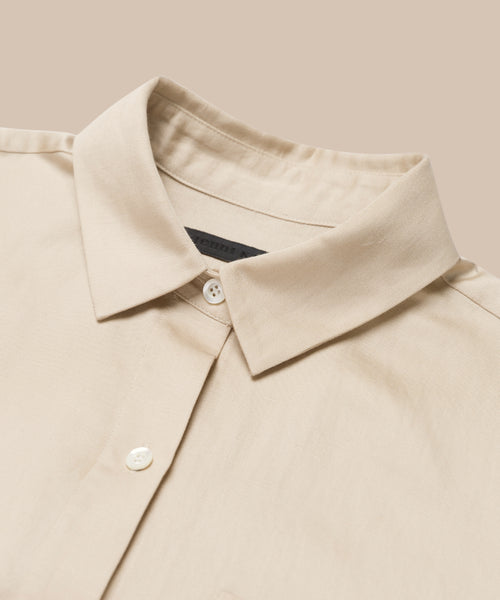 Close-up of the Madeline Shirt, a beige button-up with a classic collar and white buttons. Its subtle linen texture and soft fabric make it perfect for spring, shown here against a matching beige background.