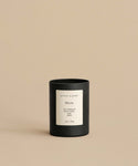 The Marin Glass Candle, hand-poured in black glass with a white label, sits on a beige surface against a matching beige background.