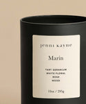 The Marin Glass Candle is a 10oz hand-poured Los Angeles candle in a cream-labeled glass jar, featuring notes of tart geranium, white floral, rose, and wood. Made from a natural wax blend and photographed against a plain beige background.