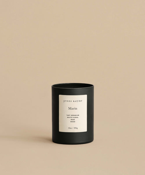 The Marin Glass Candle, hand-poured in black glass with a white label, sits on a beige surface against a matching beige background.