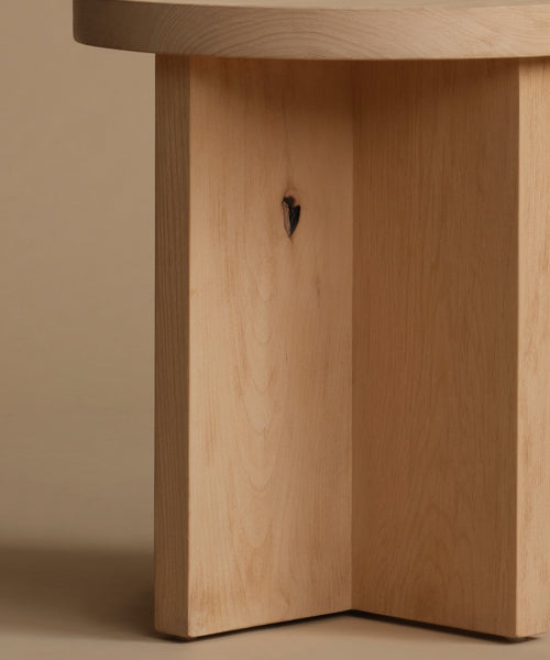 Close-up of a light natural wood table base with a small dark knot, set against a warm beige background.