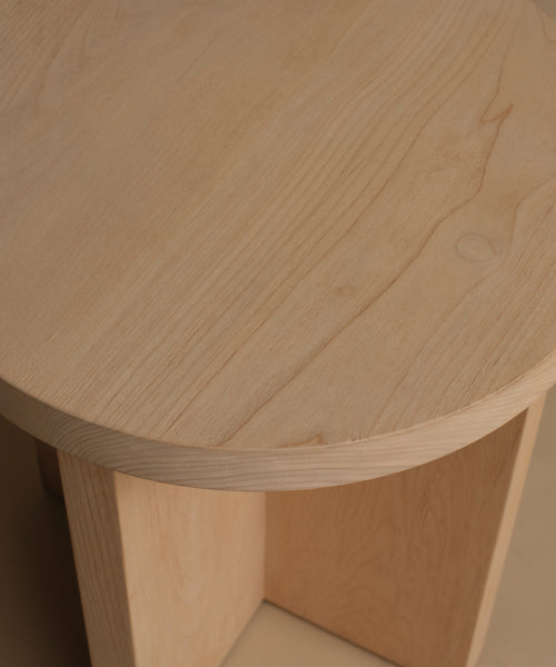 Close-up of a light natural wood side table showing the grain of the tabletop and the corner of the wooden base.