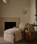 Beige armchair in a room with a fireplace and side table.