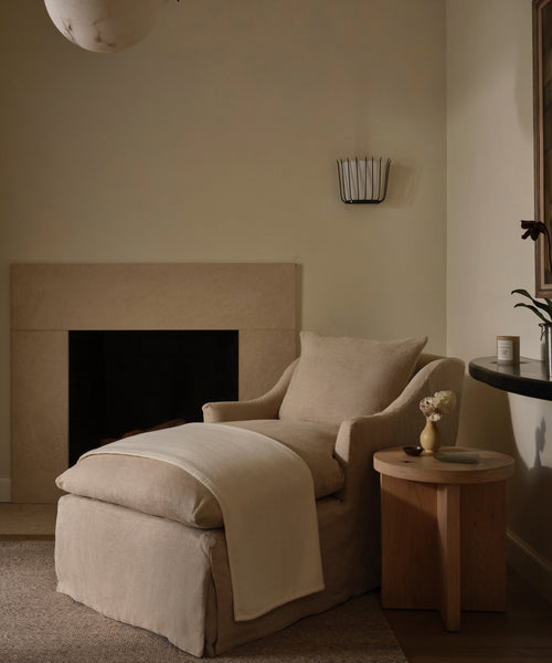 Beige armchair in a room with a fireplace and side table.