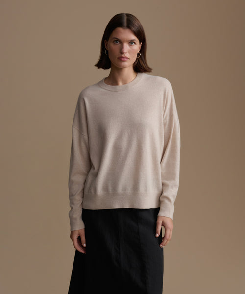 Woman wearing a beige cashmere sweater against a brown background