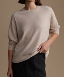 Woman wearing a beige cashmere sweater against a brown background