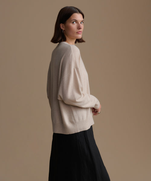 Woman wearing a beige cashmere sweater and black skirt against a brown background