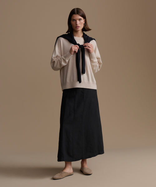 Woman wearing a beige cashmere sweater and black skirt against a brown background