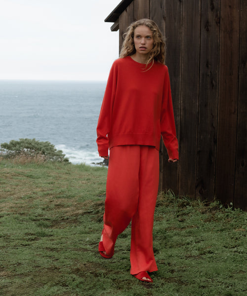 Woman in a red outfit standing by a wooden structure with ocean view