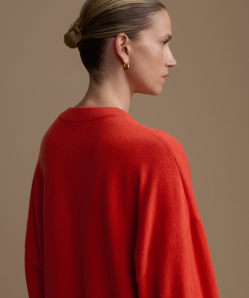 Woman wearing a red cashmere sweater against a beige background