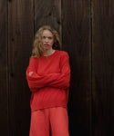 Woman wearing a red cashmere sweater and red pants standing against a wooden background
