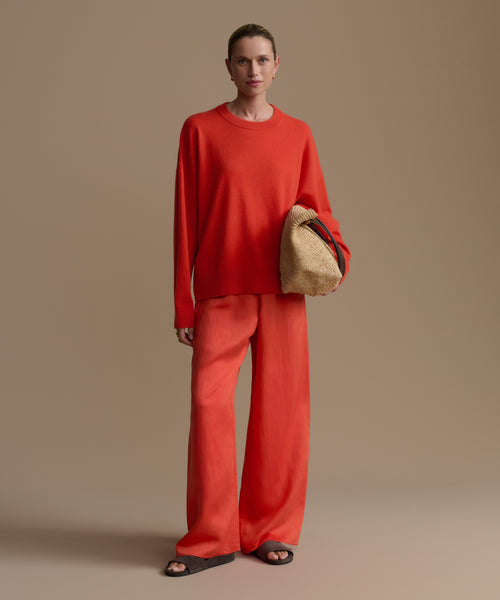 Woman wearing a red outfit holding a beige bag against a beige background