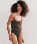 A woman with voluminous curly hair wears the Petite Square Maillot Swimsuit, made from recycled nylon with thin straps and a square neckline, standing against a plain light background.