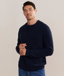 A man with short dark hair wears a navy Mens Cashmere Fisherman sweater and blue jeans against a plain light background, facing forward with a relaxed, neutral expression.