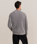A man with short dark hair stands with his back to the camera, wearing the Mens Cashmere Fisherman sweater in Heather Grey and black pants against a plain, light-colored background.