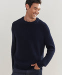 Smiling man wearing a dark blue Mens Cotton Fisherman sweater with ribbed cuffs and collar, standing with one hand in his pocket against a light background. This sweater offers a classic, lightweight knit for everyday comfort.