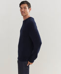 A man stands sideways, looking at the camera, wearing the Mens Cotton Fisherman sweater in navy blue and dark jeans against a plain light background.