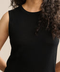 A person with long, curly dark hair wears the Merino Tank in black. The image features only their upper torso and part of their arms against a neutral background.