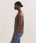 A woman in profile against a plain background wears the Merino Tank in brown and blue jeans. With her hair in a low bun and small hoop earrings, she showcases an effortlessly stylish base layer look.