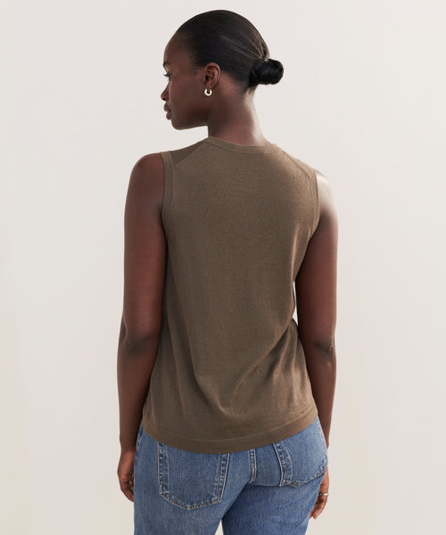 A woman with dark skin and hair in a low bun models the Merino Tank, paired with blue jeans, as she stands with her back to the camera against a plain light background.