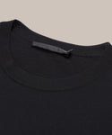 Close-up of the black Merino Tee in an oversized fit, laid flat on a neutral background, showcasing its crew neck collar and subtle black fabric label.