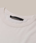 Close-up of the Merino Tee in cream, featuring a black label on the collar. Its soft, smooth merino wool stands out against a beige background—an elevated basic for effortless style.