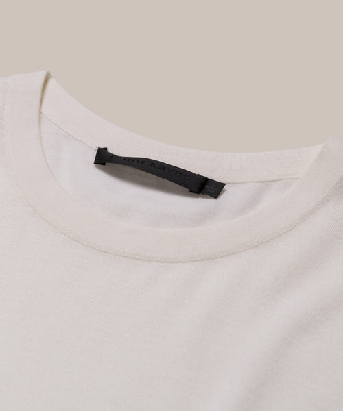 Close-up of the Merino Tee in cream, featuring a black label on the collar. Its soft, smooth merino wool stands out against a beige background—an elevated basic for effortless style.