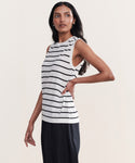 A woman with long dark hair stands sideways against a plain background, wearing the Merino Tank—sleeveless with black horizontal stripes—and black pants, posing with one hand on her hip.