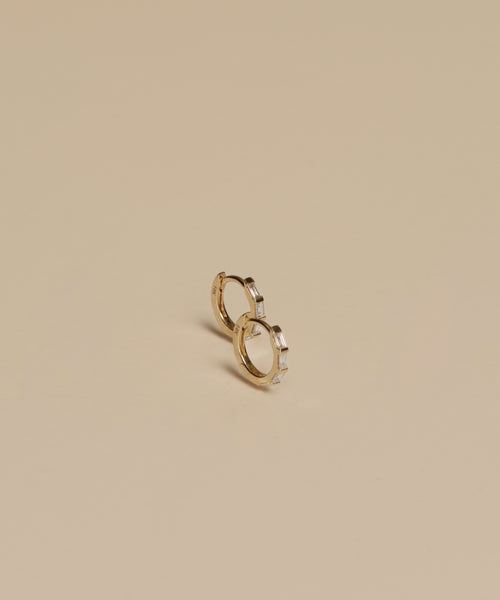 Two Merit Baguette Hoops, crafted in 14k recycled gold with rectangular gems, sit side by side on a plain beige background, highlighting their elegant design.