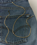 The Merit Emerald Cut Bracelet is elegantly arranged with a gold chain necklace on the back pocket of blue denim jeans.