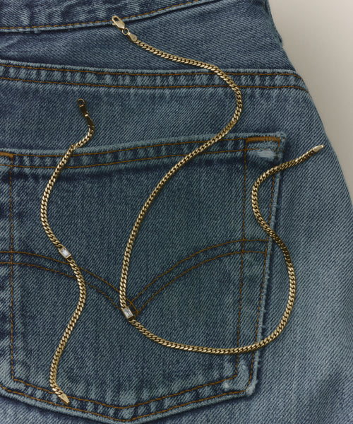 The Merit Emerald Cut Bracelet is elegantly arranged with a gold chain necklace on the back pocket of blue denim jeans.