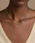 A person wearing the Merit Emerald Cut Necklace, featuring a 14k gold chain and small square pendant, shown from the shoulders up in a light beige V-neck top.