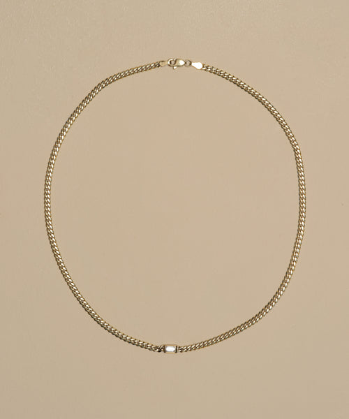 The Merit Emerald Cut Necklace, crafted in 14k gold with a small rectangular clasp, is displayed in a circular arrangement on a beige background.