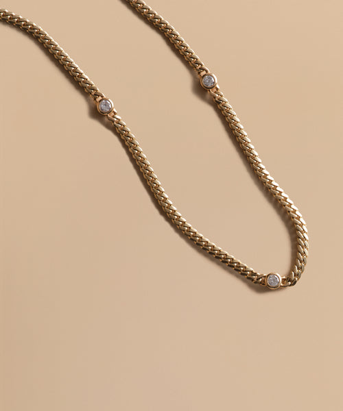 The Merit Round Cut Diamond Necklace by Jenni Kayne features three evenly spaced round diamonds set in 14k gold, elegantly displayed on a smooth beige background.