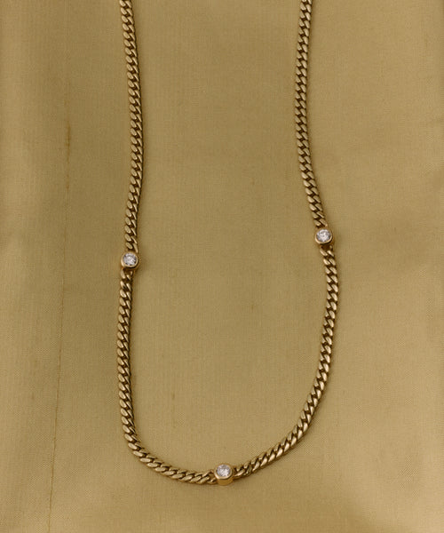 The Merit Round Cut Diamond Necklace features three evenly spaced round diamonds set in 14k gold, shown against a light gold fabric background—a timeless design inspired by Jenni Kayne jewelry.