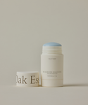 A white tube of Microbiome Balancing Deodorant with a blue cap, labeled as aluminum-free and ideal for sensitive skin. The cap, placed beside it, partially displays Oak Ess against a plain, light background.