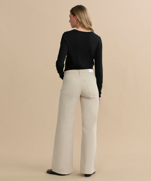 A woman faces away from the camera, wearing a black long-sleeve top and the Mid Rise Wide Leg pants, against a plain beige background.