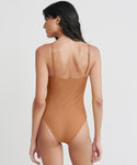 Woman with long dark hair, seen from the back, wearing the Malta One Piece Swimsuit in terracotta, standing against a plain white background.